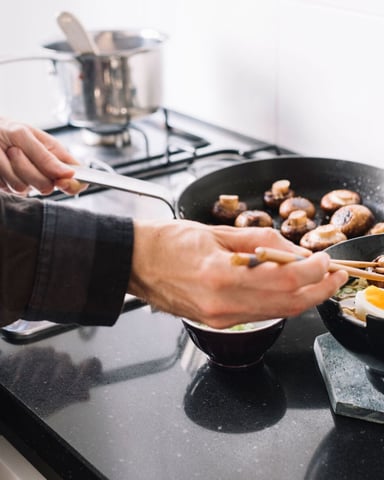 Hands assembling a ramen bowl at a home stove