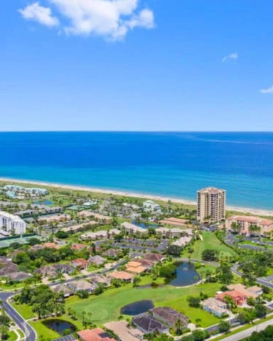 Aerial view of beachfront residential community with high-rise and mid-rise buildings, homes, landscaped grounds, and turquoise ocean.