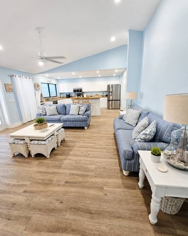 Open-plan living room and kitchen with blue striped seating, wood flooring, and vaulted ceiling with skylights
