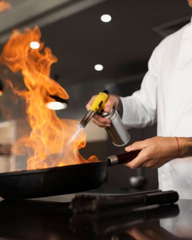 Chef flambéing a pan with a blowtorch